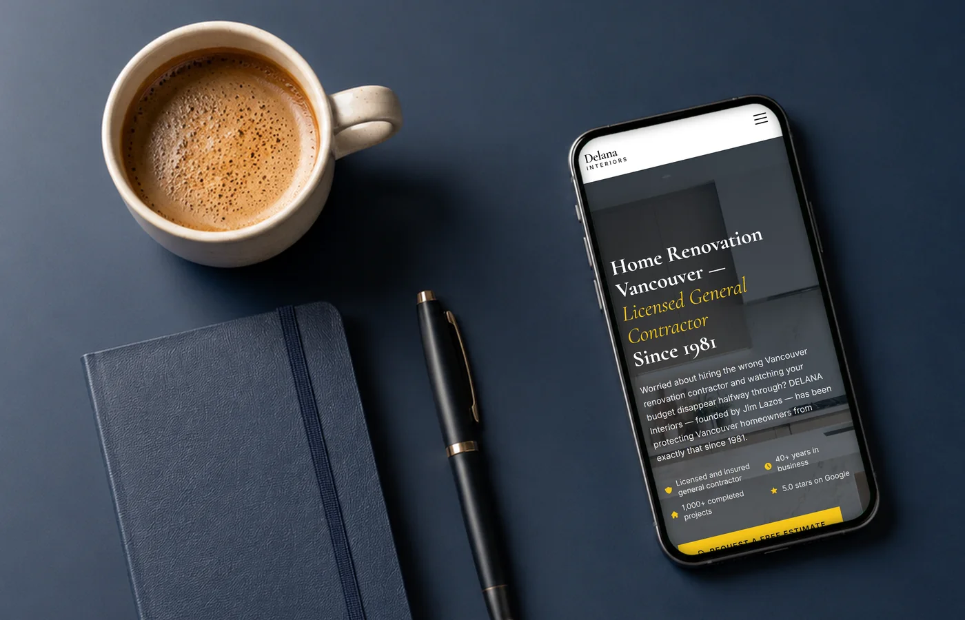 The DELANA Interiors website open on a phone beside a coffee cup and notebook — mobile-first web design by IshaanEx Digital